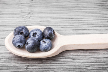 Blueberries on wooden spoon placed on gray wooden table.