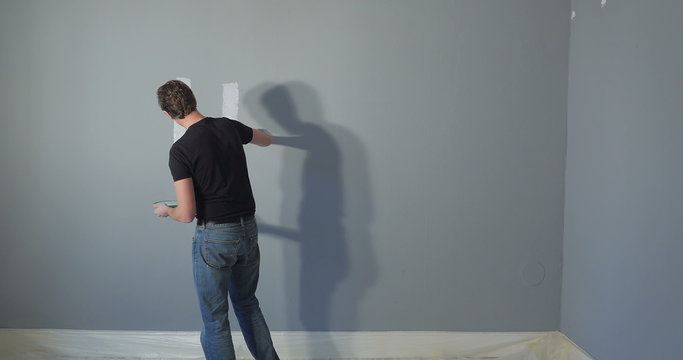 person painting the words HOME on a wall in his new appartment. The colour of the wall is light grey with a blue touch.