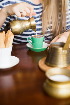 Woman pouring milk from vintage brass jug into coffee. Selective focus.