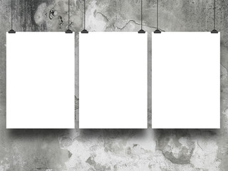 Close-up of three hanged paper sheets with clips on stained and weathered concrete wall background