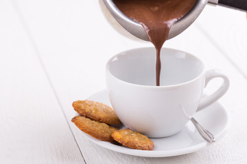 Pouring tasty hot chocolate in white cup on table.