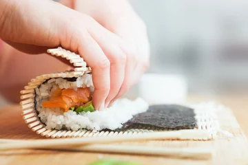 Selbstklebende Fototapeten Sushi vorbereiten, rollen. Lachs, Avocado, Reis und Stäbchen auf Holztisch. © Photocreo Bednarek