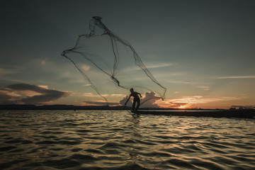 Fisherman throwing net at sunset