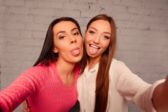 Happy funny girlfriends make selfie photos and showing tongue