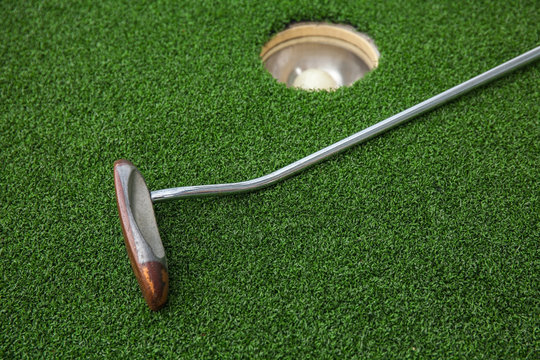 Putting golf club on green grass with golf ball in the hole 