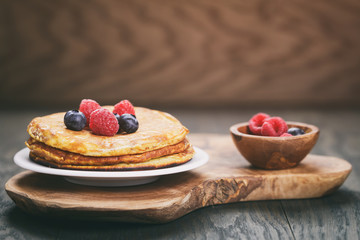 Pancakes with berries on wood table, vintage toned