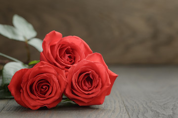 three red roses on wooden table, shallow focus