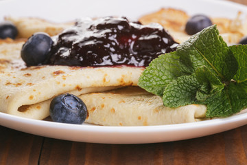 homemade blinis or crepes with blueberries and jam on wooden table, vintage toned