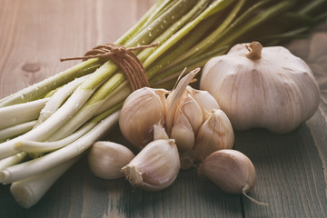 fresh green spring onion tied with twine and garlic on old table, vintage toned