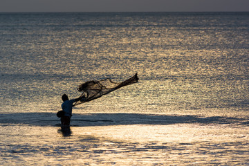 Fischer auf Bali steht im Wasser und wirft sein Netz aus im Gegenlicht