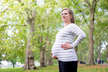 Happy and young pregnant woman in park in summer