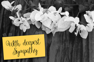 "With deepest sympathy" note with flowers on old wooden backgrou