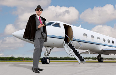 Handsome business man on the steps of a private jet wearing a hat and smoking a cigar