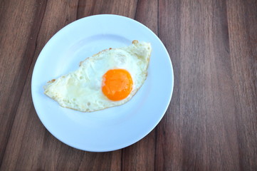 Top view of white dish with fried egg on wooden background.