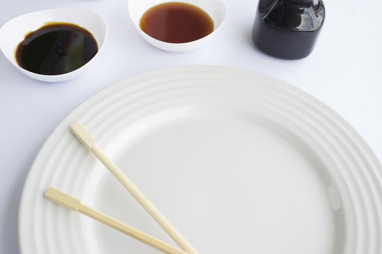 Plato blanco con palillos chinos acompañado de salsa de anguila y de soya