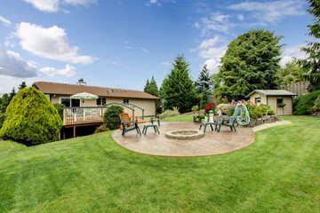Fototapeta premium Large back yard with grass, circular patio, chairs, and garden.