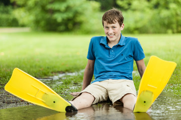 Happy teenager sitting in large puddle