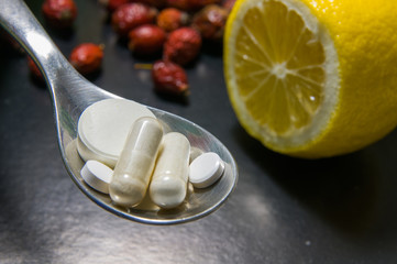 Pills in a spoon versus lemon with hips selective focus on pills