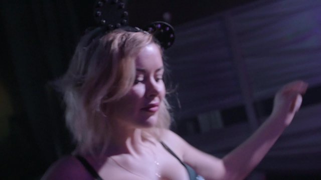 Dj girl in glow top, mouse ears dance, shake breast at turntable in nightclub. 