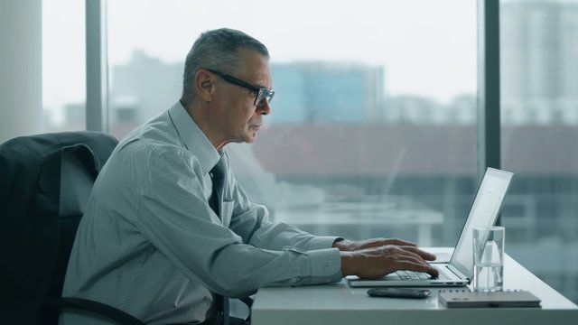 elderly businessman working with computer in modern office. his back is hurts