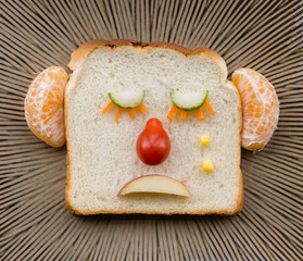 Funny sad bread face made with fruit and vegetables on ceramic plate