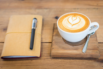 Hot latte art coffee cup on wooden table and note book, vintage
