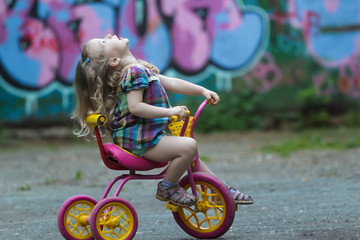 Preschooler girl wearing checked tunic riding yellow and pink tricycle