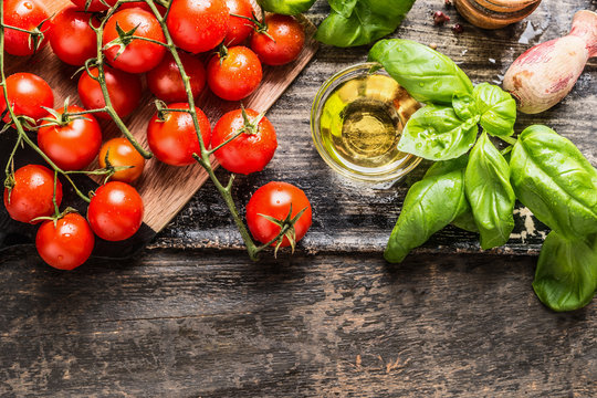 Cherry Tomatoes, basil and olive oil on wooden background, top view. Italian food cooking ingredients.
