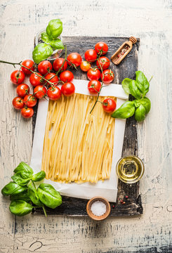 Top view of  Fettuccine pasta with tomatoes, basil leaves and olive oil on rustic background.  Italian food cooking ingredients.