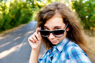 beautiful girl in black sunglasses on the road between the green