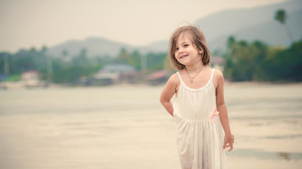 Young happy girl in white dress is walking on the tropical beach