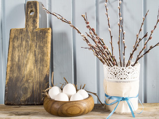 White eggs in the bowl, willow branches and wood cutting board o