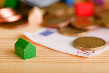 Small green toy house in front of coins and bills