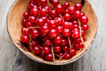 Redcurrant on a branch close to a wooden bowl.