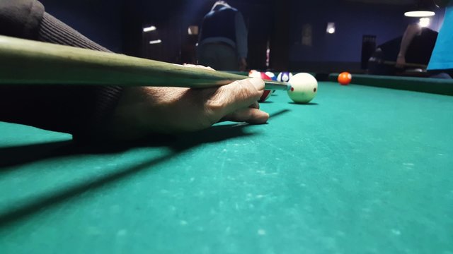 Action camera over the eight ball pool table follow the hand of a player missing the ornage ball number 5 with a soft shot from billiard pocket in an eight ball game