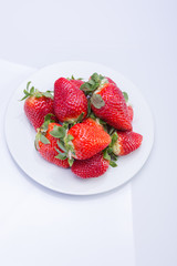 Strawberry red on a white plate and a white background, a bright image with contrast. side view, top. summer red berries. a series of color photographs