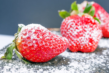 large red strawberries in white powdered sugar on a stone gray background, contrast color image with space for text. sophisticated look berries.