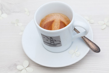 A cup of hot strong espresso on a white wooden table decorated with white hydrangea flowers