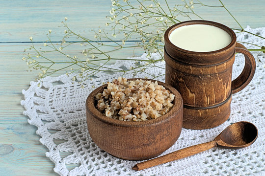  Buckwheat porridge and milk.
 Buckwheat porridge in a wooden bowl and milk in a wooden mug on a napkin on a blue wooden background.
