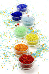 Row of glass bowls full of multicolored beads on white background