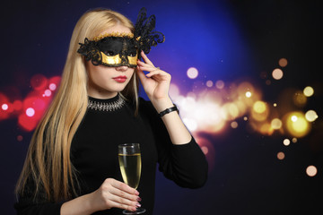 cheerful girl with a glass of champagne and carnival mask on a background of bright lights