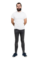 Happy bearded man with hands behind back in white t-shirt and tight jeans looking at camera. Full...