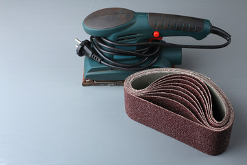 Vibratory sander with sandpaper on grey wooden table - obrazy, fototapety, plakaty