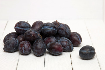 Tasty purple plums isolated on a white wooden background.