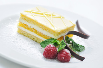 sponge yellow cake with fruit and chocolate decoration on white plate, sweet dessert, patisserie, shop