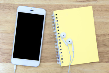 Phone and notebook with blank screen on wooden background.