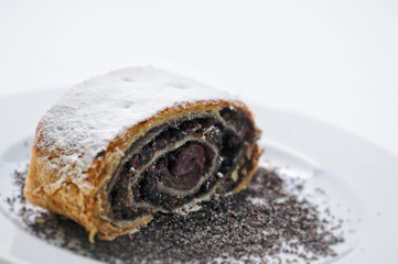 sweet poppy strudel with powder sugar on white plate, product photography for bakery or patisserie