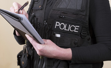 Police officer wearing tactical vest writing notes on a pad
