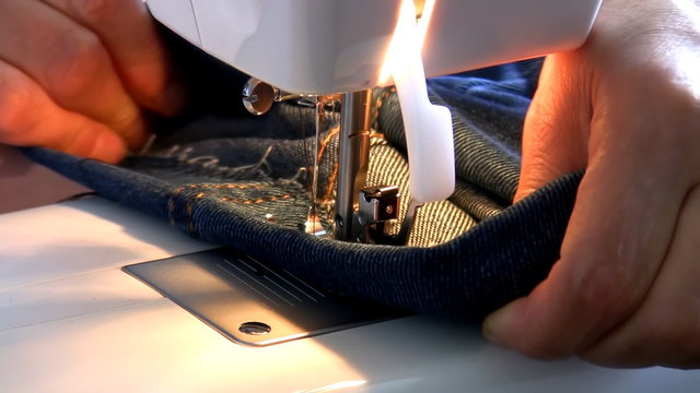 Close up of hands repairing denim jeans using electric sewing machine