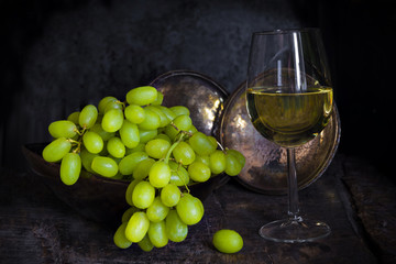 Green grapes and a glass of white wine on dark background - vintage, moody style